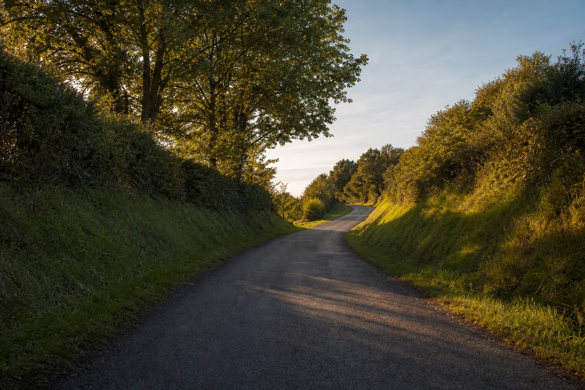 Route de campagne en légère montée sous une lumière rasante de fin de journée